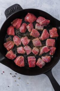 Partially cooked steak tips searing in a cast iron skillet.