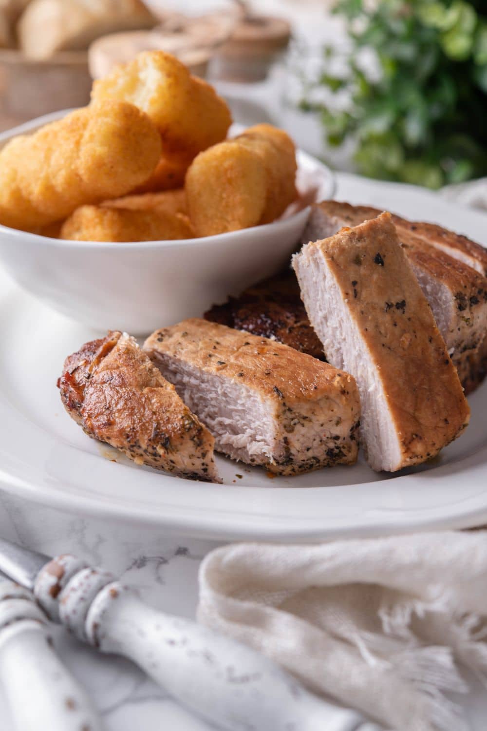 Thick cut pork chops sliced into thick pieces, served on a plate with a side of tater tots in a small bowl.