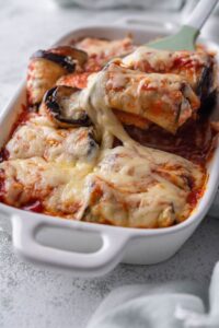 Eggplant rollatini in a casserole dish topped with melty, stretchy cheese.