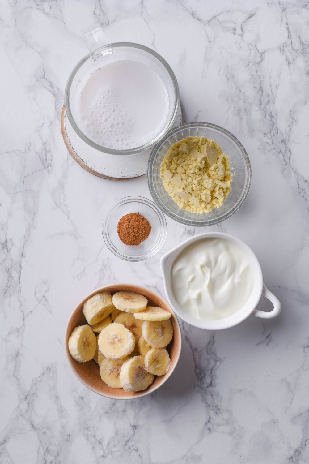 A glass of milk, a cup of protein powder, a bowl of cinnamon, a cup of yogurt.