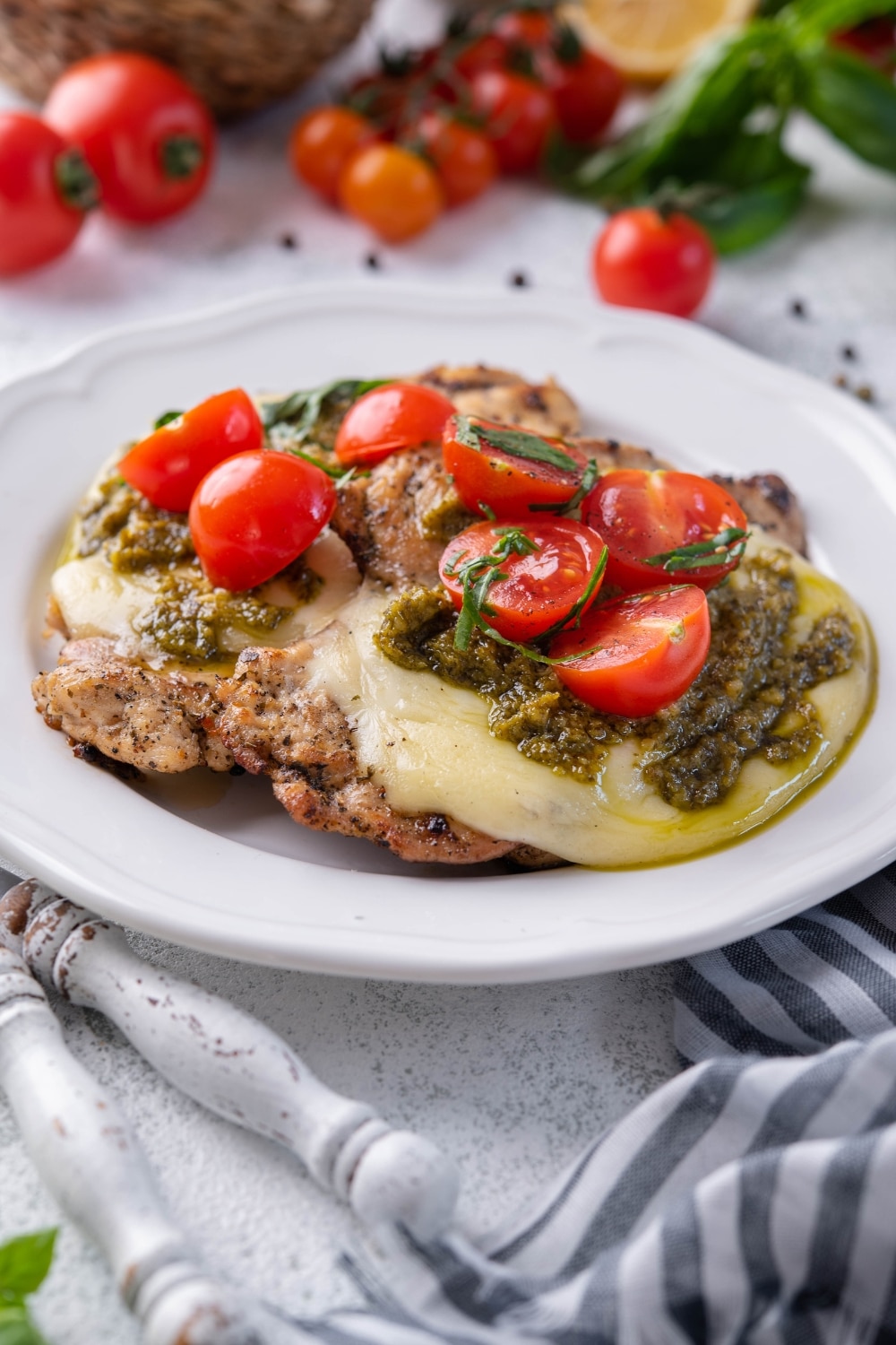 Grilled chicken margherita topped with mozzarella, pesto, and cherry tomatoes on a white plate.