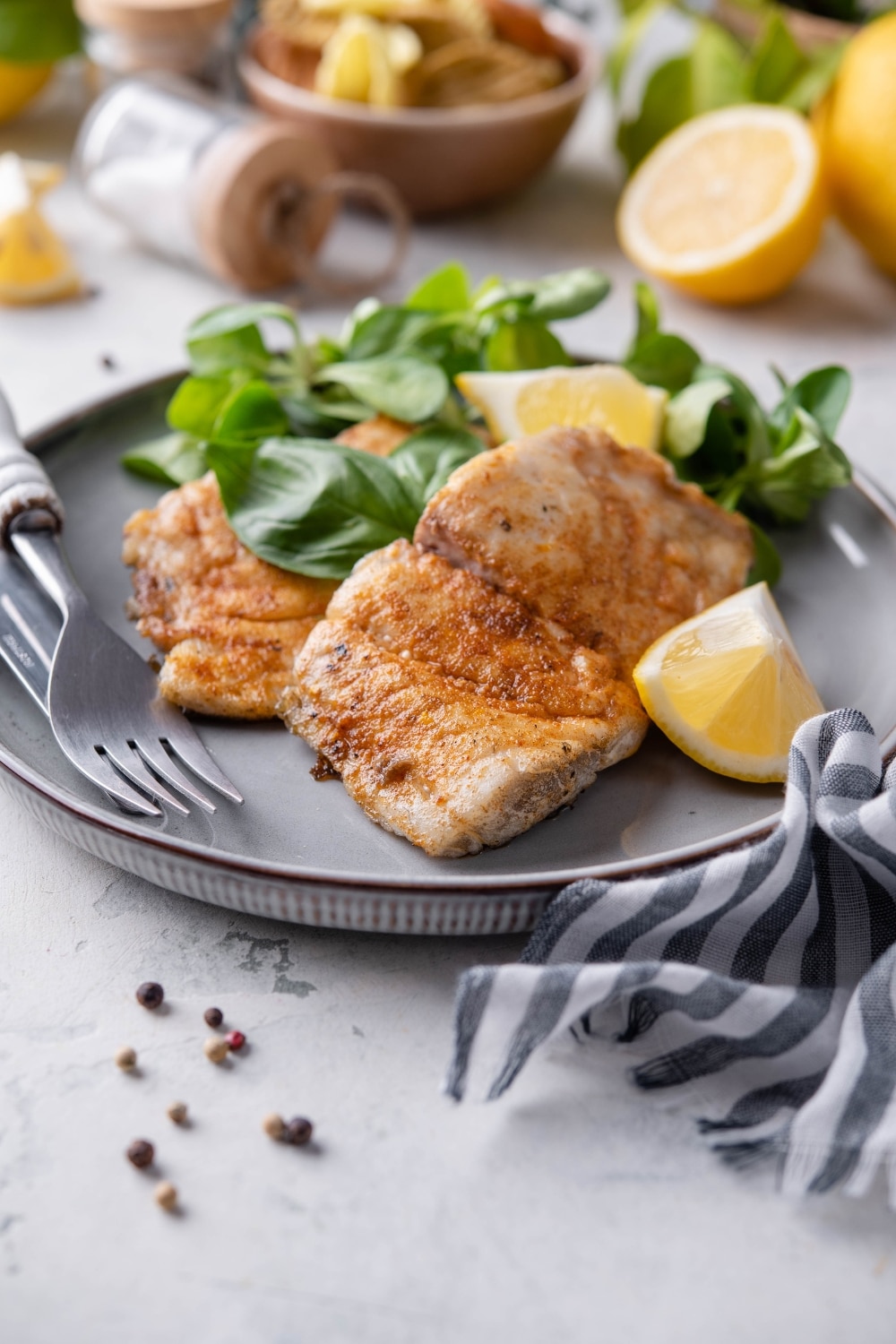 Two grilled halibut filets with lemon wedges and a side of salad, all on a grey plate.