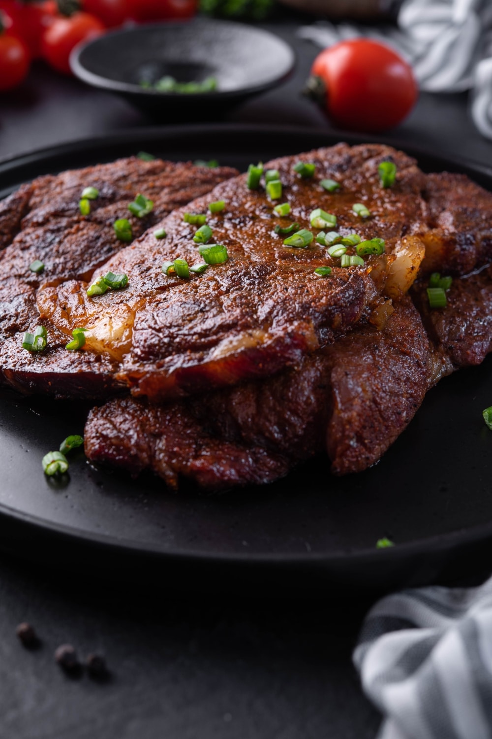 Two grilled ribeye steaks on a black plate garnished with chopped spring onions.