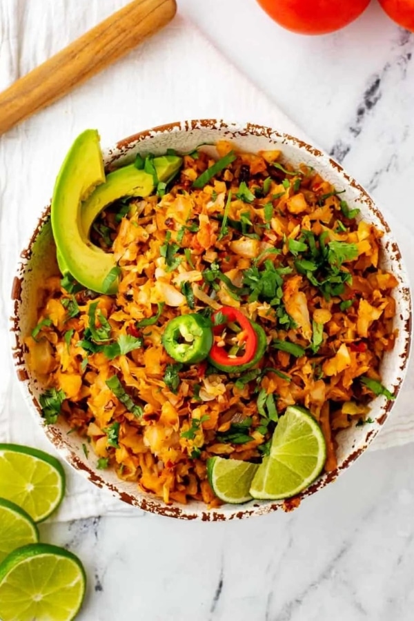 A bowl of seasoned cabbage rice with lime and avocado.