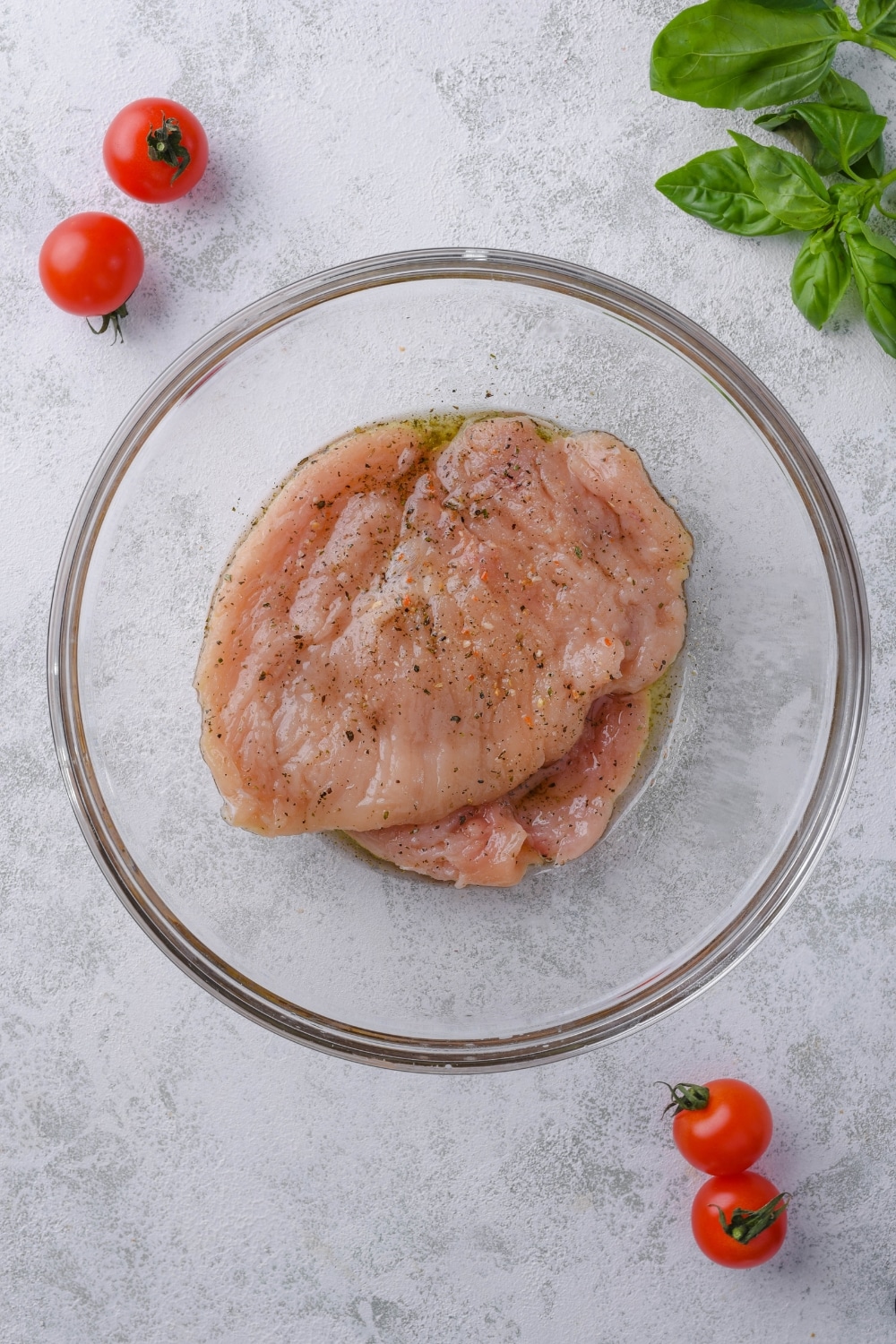 A glass bowl of raw chicken breast filets covered in seasoning.