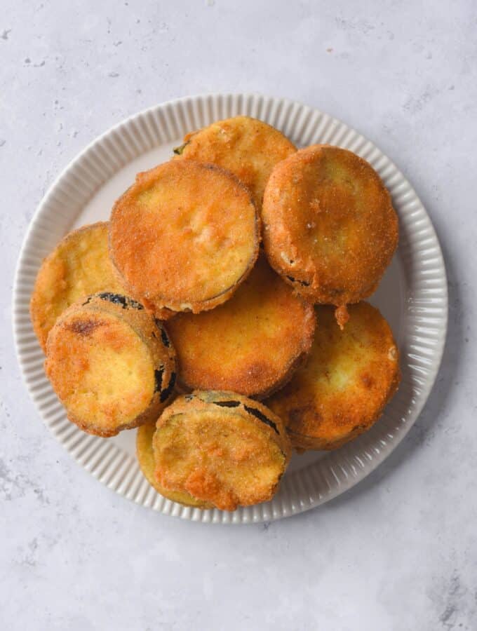 A bunch of fried eggplant slices on top of a white plate on a counter.