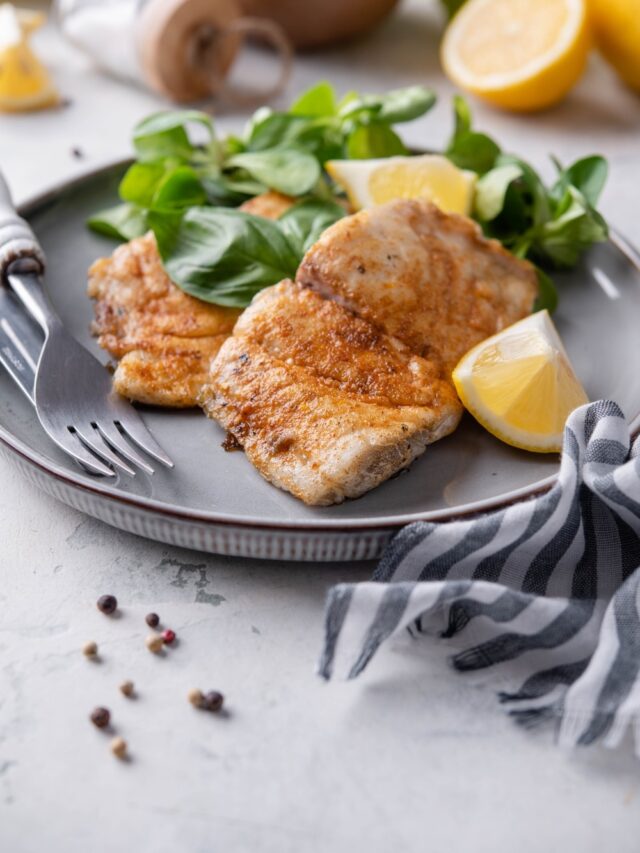 Two grilled halibut filets with lemon wedges and a side of salad, all on a grey plate.