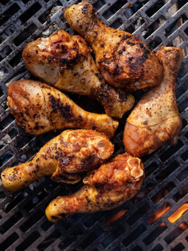 Seasoned chicken drumsticks cooking on a charcoal grill.