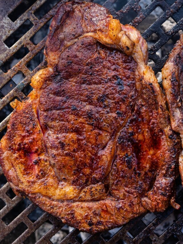 A grilled ribeye steak cooking on a charcoal grill.