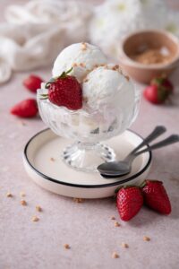 Frozen yogurt ice cream scoops topped with a fresh strawberry and crushed hazelnut brittle.