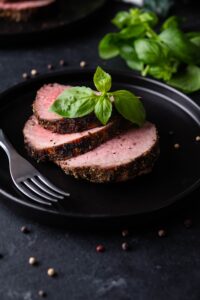Sliced medium rare grilled beef tenderloin garnished with basil and served on a black plate.
