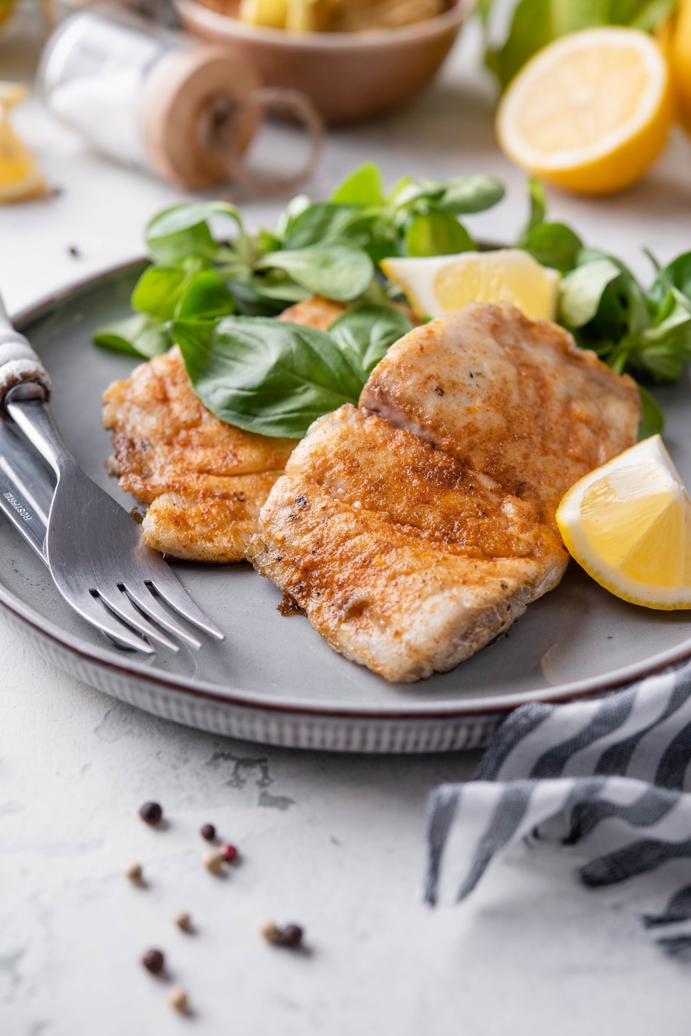 Two grilled halibut filets garnished with lemon wedges and served with salad greens.