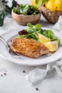 A grilled mahi mahi filet served with salad greens and lemon wedges with a small bowl of salad greens in the back.