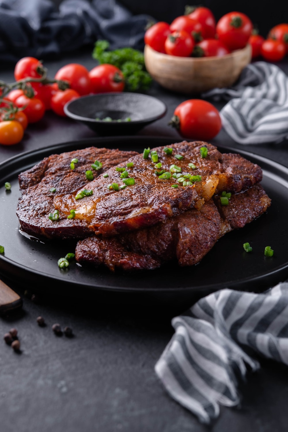 Two grilled ribeye steaks garnished with chopped spring onions and served on a black plate.