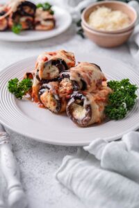 Eggplant rollatini garnished with parsley served on a white plate.
