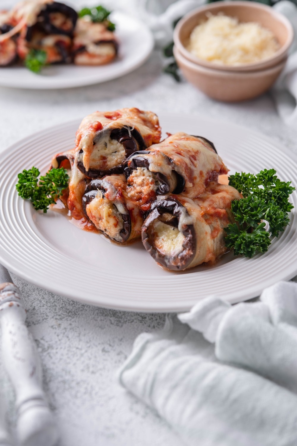 Eggplant rollatini garnished with parsley served on a white plate.