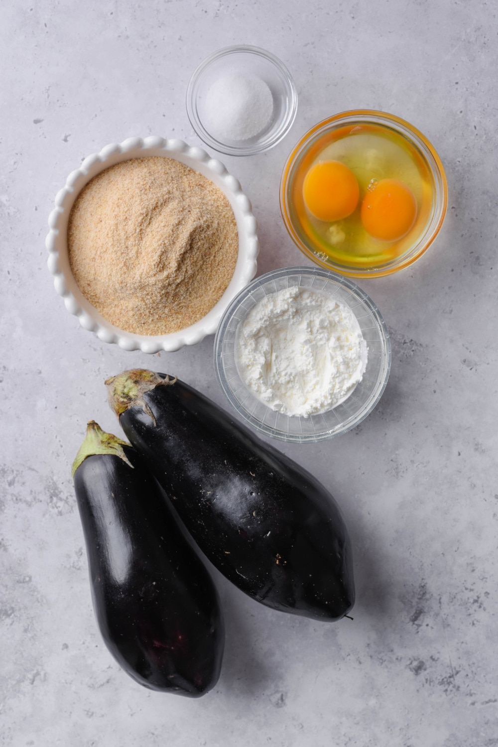 Two large eggplants and bowls of breadcrumbs, cornstarch, eggs, and salt.