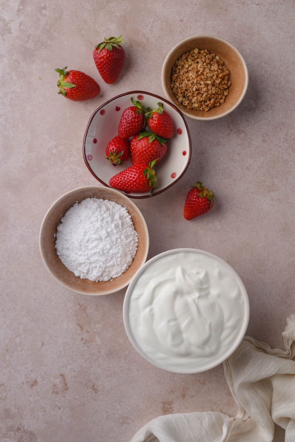 Bowls of greek yogurt, powdered sugar, fresh strawberries, and ground hazelnut brittle.