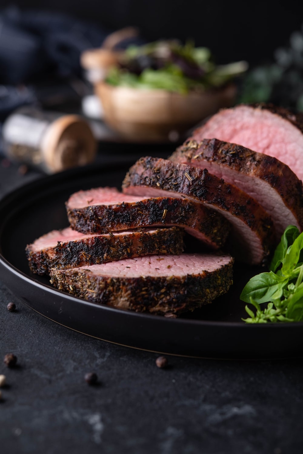 A closer look at sliced medium rare grilled beef tenderloin on a black plate.