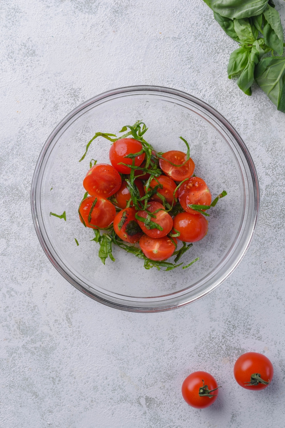 A glass bowl of sliced cherry tomatoes tossed with sliced basil leaves, lemon juice, salt, and pepper.