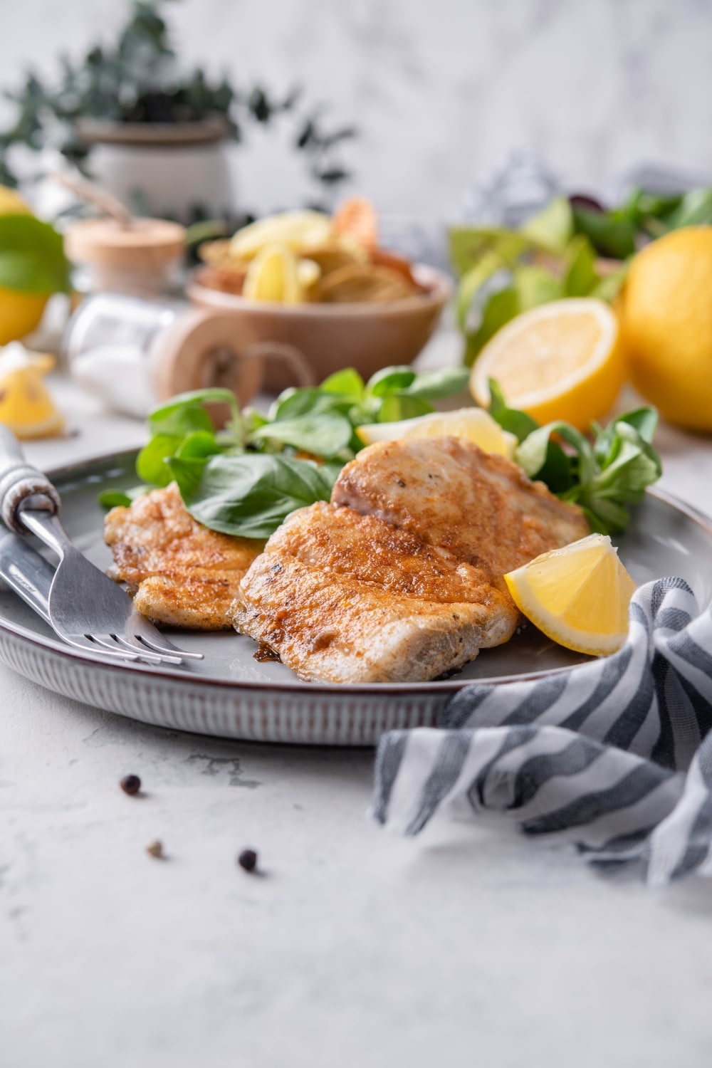 Two grilled halibut filets served with salad and lemon wedges on a grey plate.