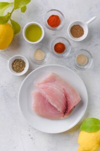 A plate of raw mahi mahi filets next to small bowls of spices and olive oil.