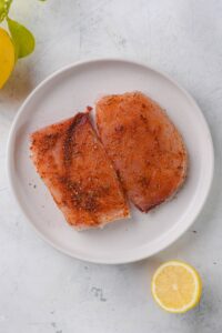 Two seasoned raw mahi mahi filets on a white plate.