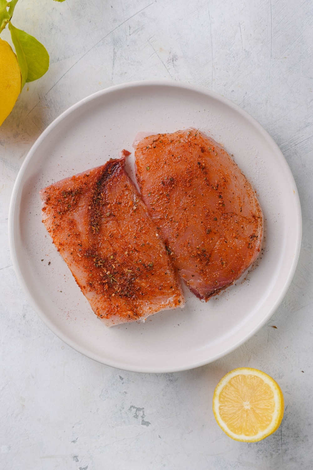 Two seasoned raw mahi mahi filets on a white plate.