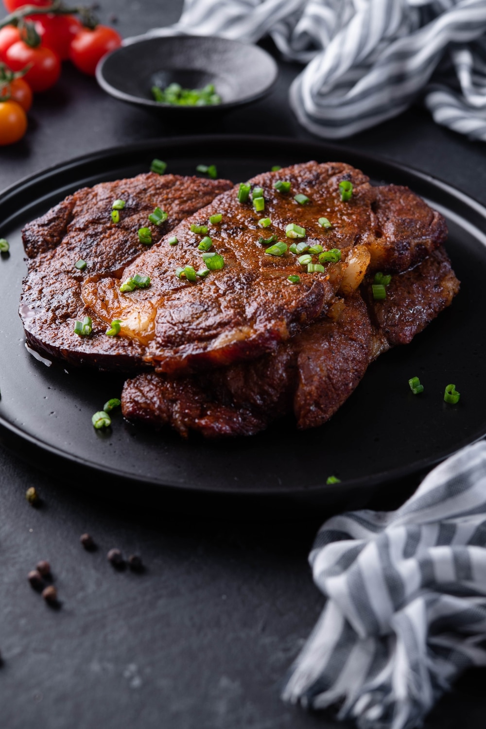A closer look at grilled ribeye steaks garnished with spring onions on a black plate.