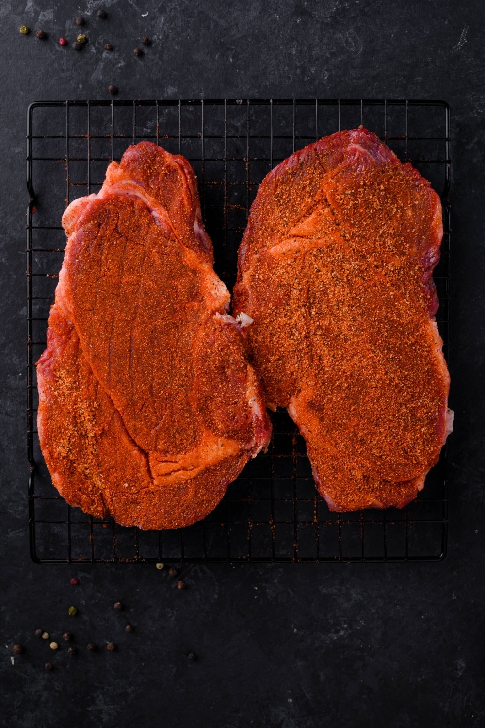 Two raw ribeye steaks coated in steak rub.