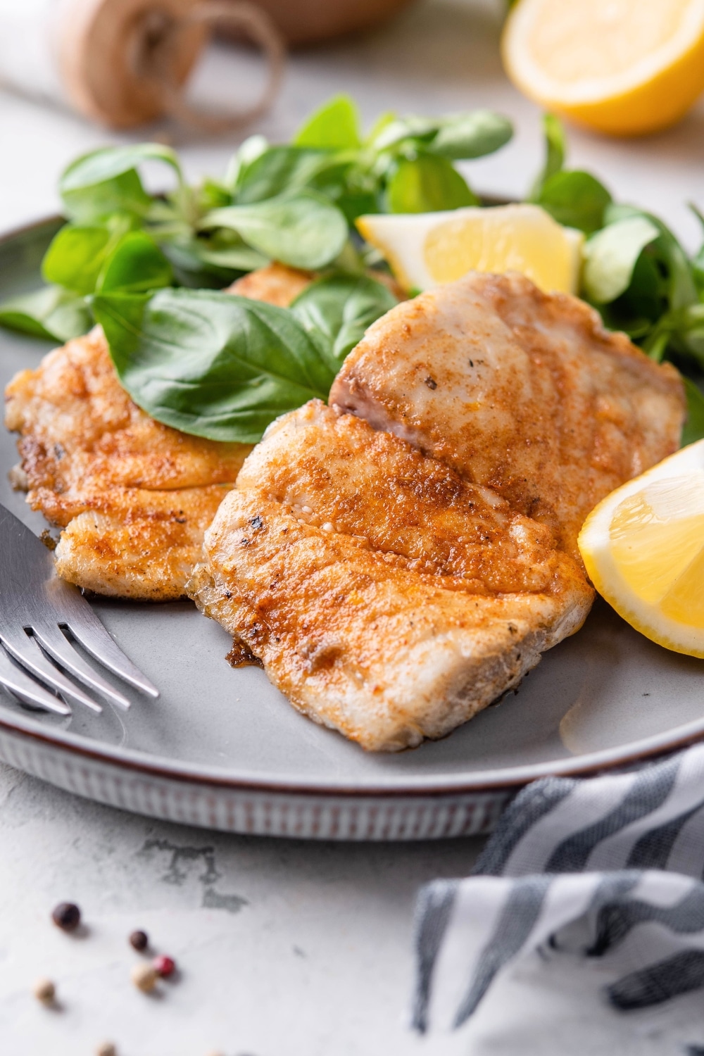 Three pieces of grilled halibut on a plate with lemon wedges and lettuce.