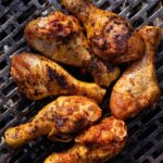 Six seasoned chicken drumsticks on a charcoal grill.