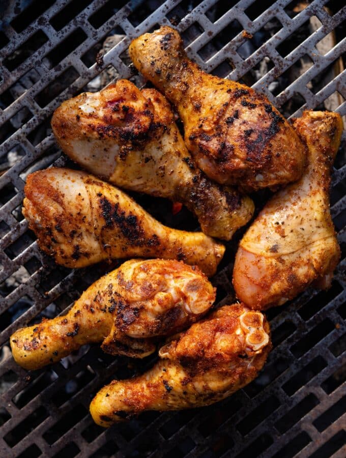 Six seasoned chicken drumsticks on a charcoal grill.