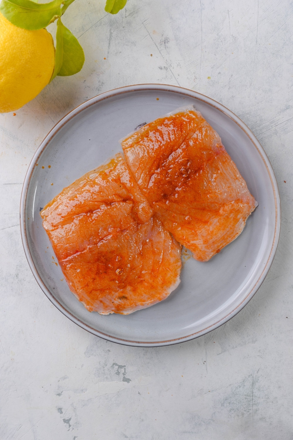 Two seasoned raw halibut filets on a grey plate.