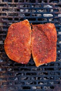 Two seasoned mahi mahi filets cooking on a charcoal grill.