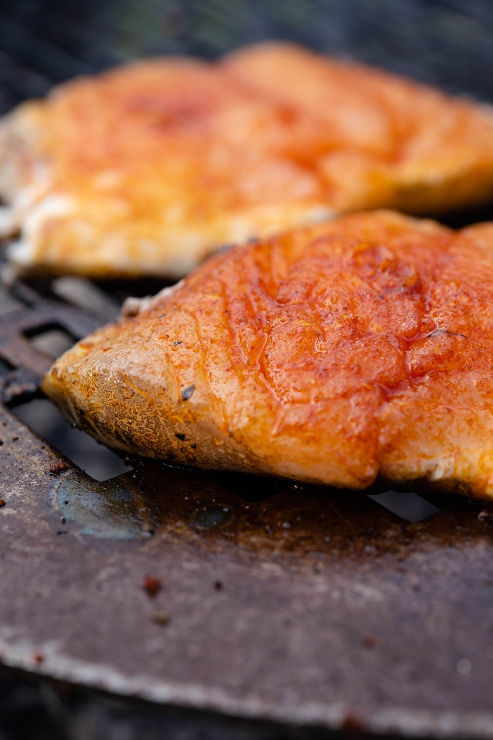 Close up of seasoned halibut filets on a charcoal grill.