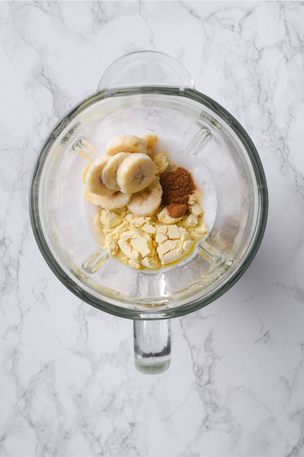 Frozen bananas, cinnamon, vanilla protein powder, and milk in a blender.