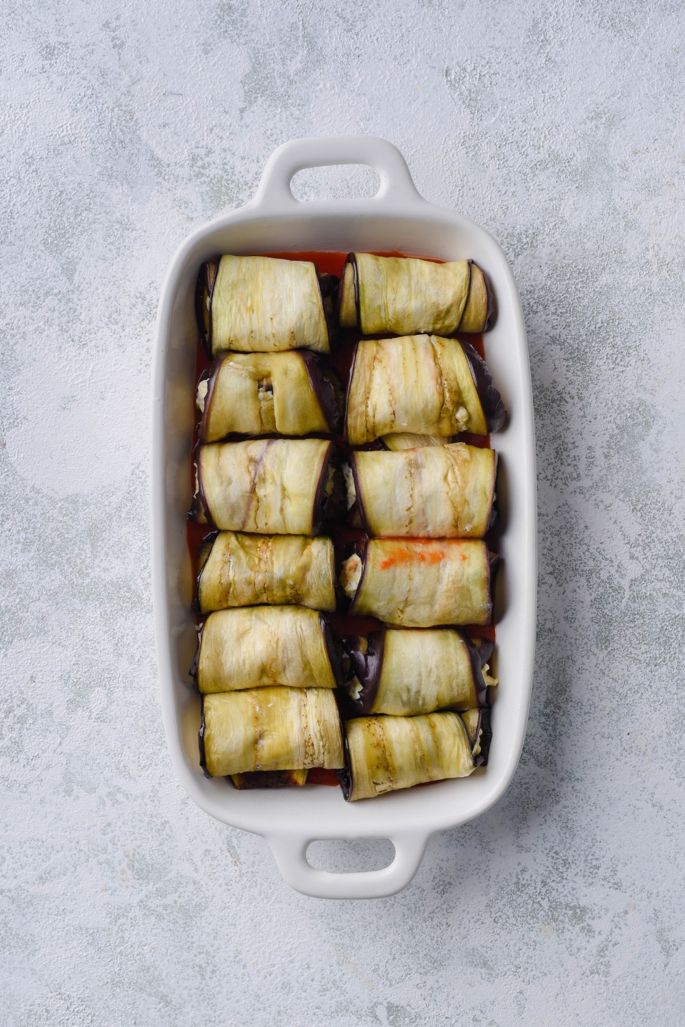 Rolled stuffed eggplant arranged in a rectangle casserole dish.