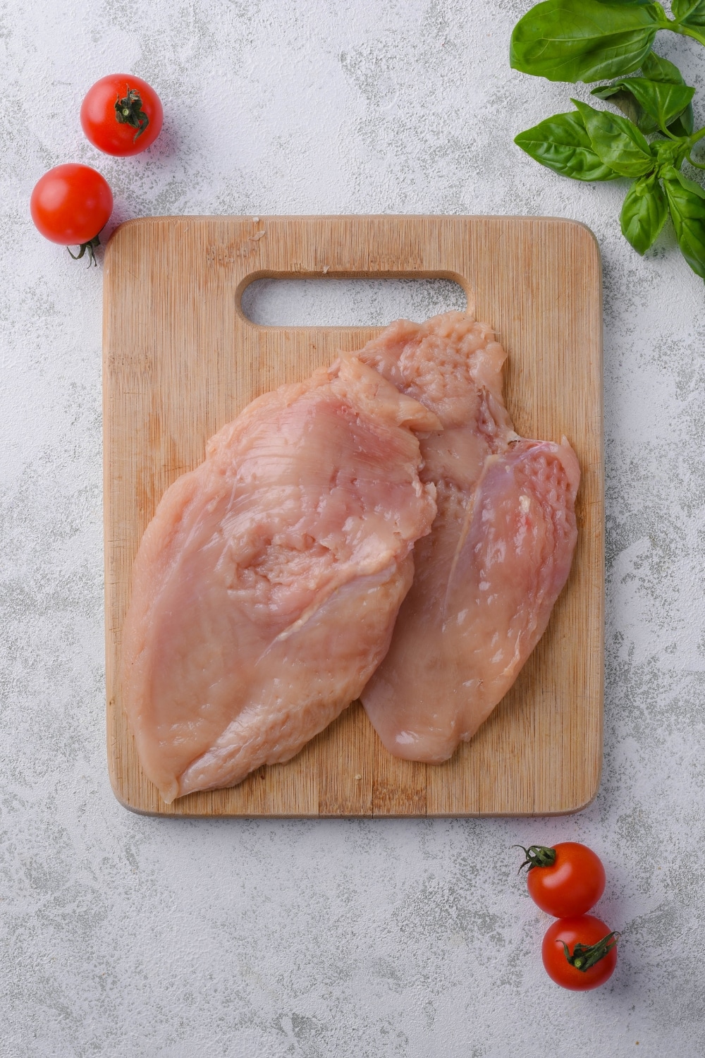 Two pounded raw chicken breast filets on a wooden cutting board.