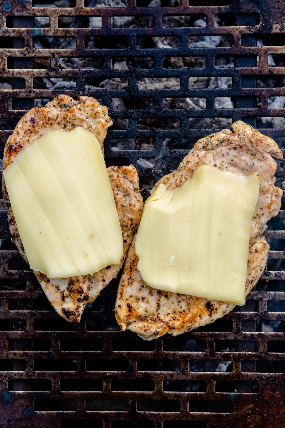 Two cooked chicken breast filets on a grill, topped with mozzarella slices.