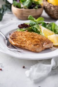 A plate of grilled mahi mahi filet served with salad greens and lemon wedges next to a small bowl of salad greens.