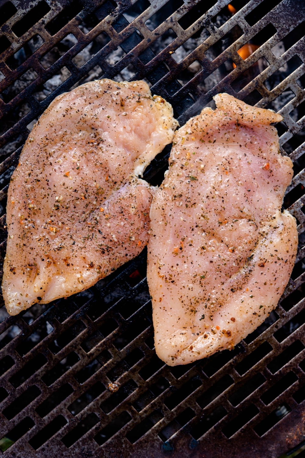 Two pounded raw chicken breast filets on a grill.