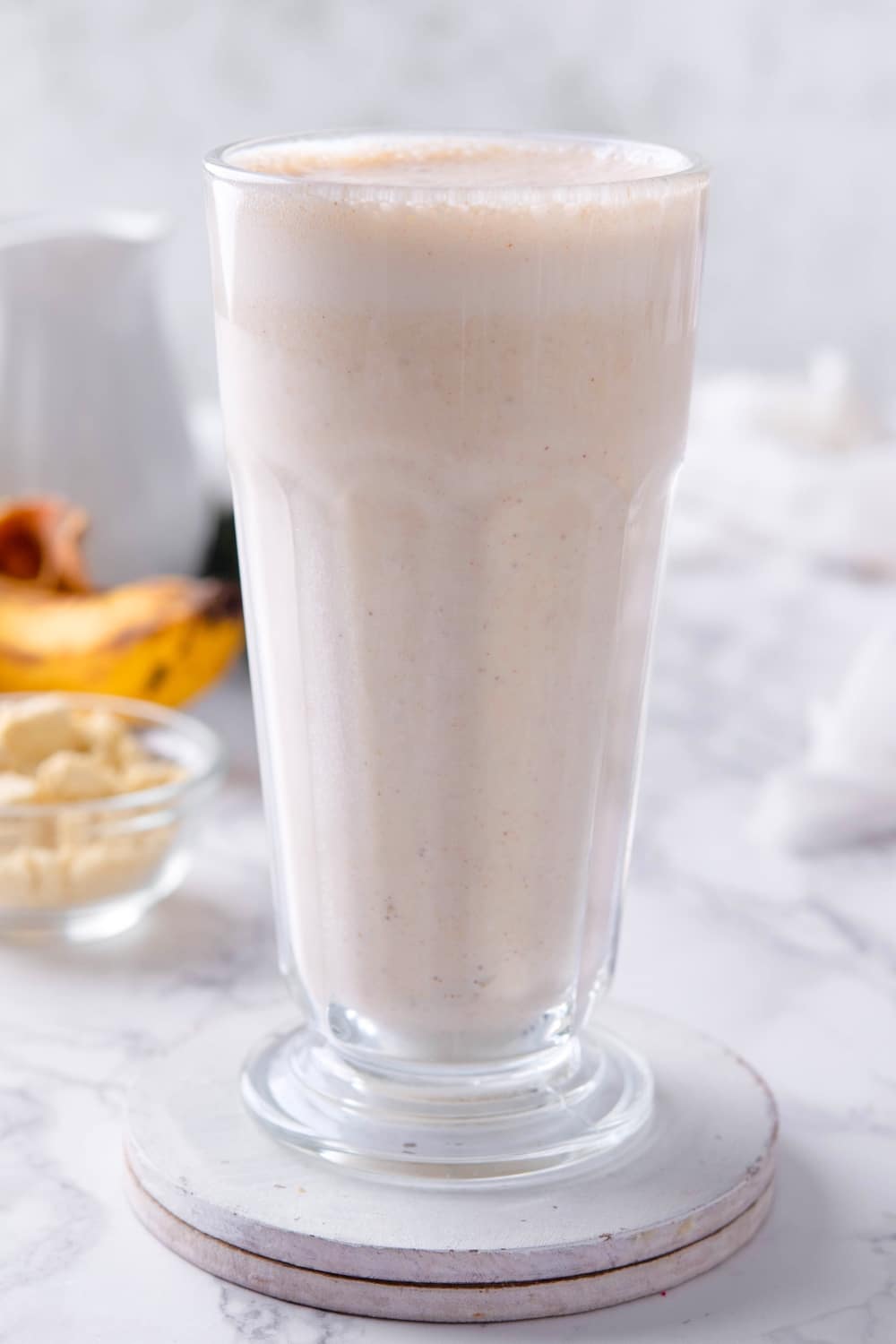 A tall glass that is filled to the top with a banana protein shake.