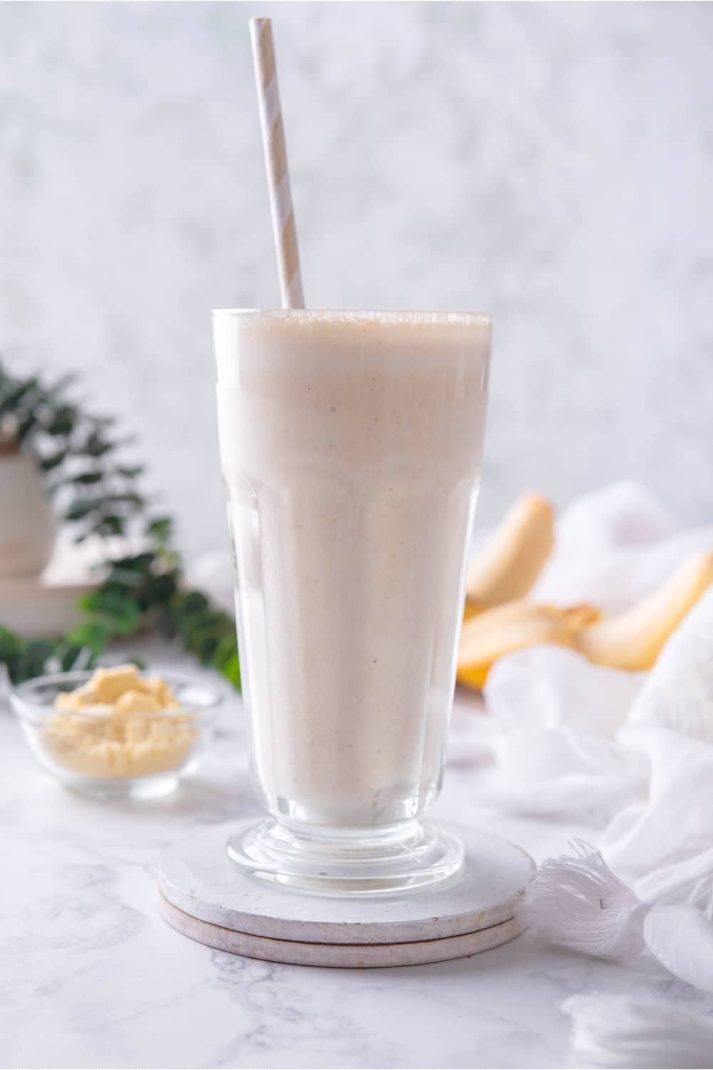 A straw in a glass that has a banana protein shake in it.