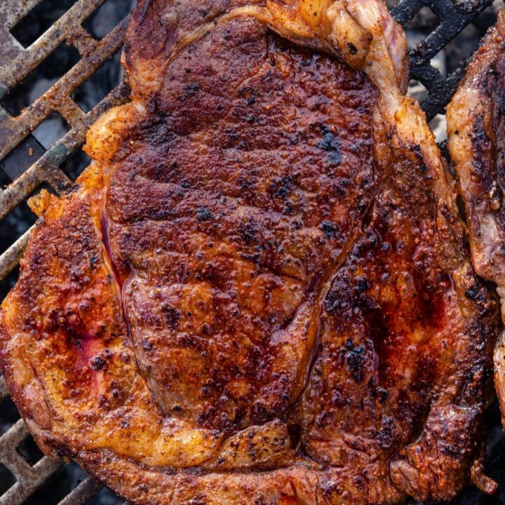 A grilled ribeye steak cooking on a charcoal grill.