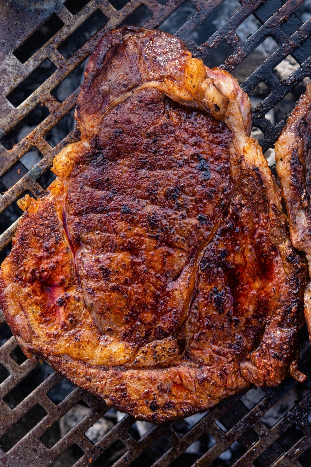 A grilled ribeye steak cooking on a charcoal grill.