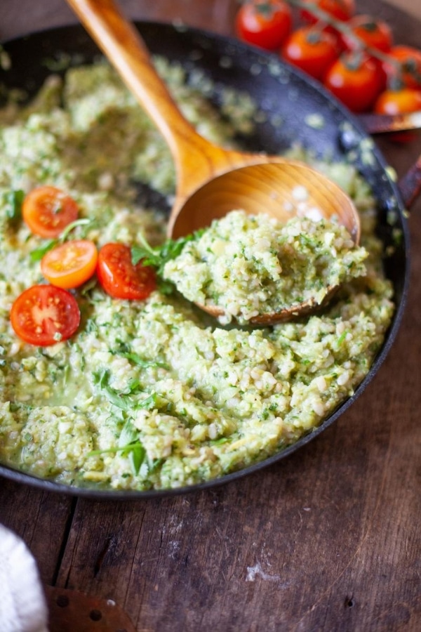 A wooden spoon with zucchini rice and cauliflower rice on it in a skillet with the rice.