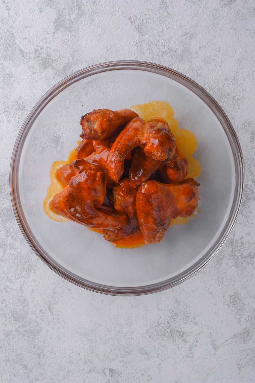 Baked chicken wings coated in wing sauce in a glass bowl.