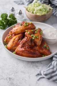 Baked chicken wings on a plate garnished with chopped green onions and served with ranch.