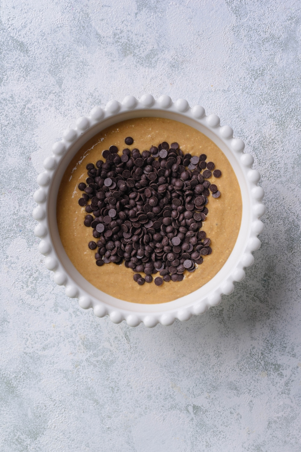 Banana bread batter topped with chocolate chips in a white bowl.